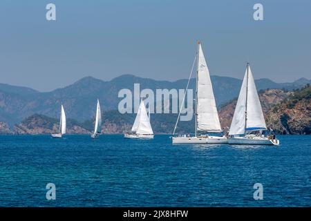 Eine Flotte von Segelyachten manövriert in der Ägäis vor der türkisfarbenen Küste in der Nähe der Hafenstadt Fethiye. Stockfoto