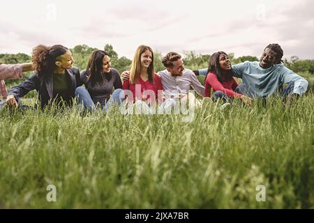 Multirassische internationale Gemeinschaft von glücklichen Freunden, die auf grüner Wiese sitzen - multiethnische Universitätsstudenten, die Spaß daran haben, sich auf dem Gras auszuruhen Stockfoto