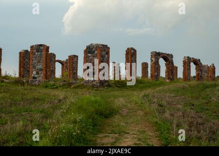 Die Überreste einer Steinsäule aus einem alten Gebäude in der Mitte eines Feldes an einem sonnigen Frühlingstag. Stadt Smiltene, Lettland. Altes ziegelsteingebäude aus stonehenge. Stockfoto