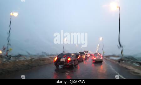 Im Auto. Nahaufnahme Regen Wassertropfen. Auto Windschutzscheibe Blick während regnerischen Tag auf der Autobahn am Abend. Stockfoto