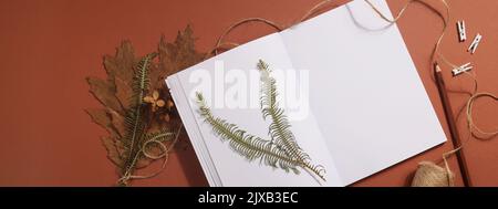Getrocknetes gepresstes Blatt auf Papier aus Notizbuch mit Bleistift, Schere und Garn auf braunem Hintergrund. Hobby, Handarbeit, Blumenkunst und Boho-Konzept. Banner Stockfoto