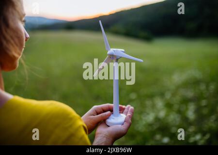 Nahaufnahme der Hände mit Modell des Windturibe in der Natur. Konzept der ökologischen Zukunft und nachwachsenden Ressourcen. Stockfoto