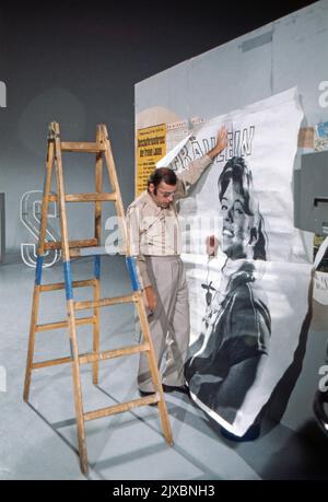 Chris Howland, britischer Schlagersänger, Schauspieler, Fernseh- und Radiomoderator, hängt ein Plakat auf, Deutschland 1975. Stockfoto