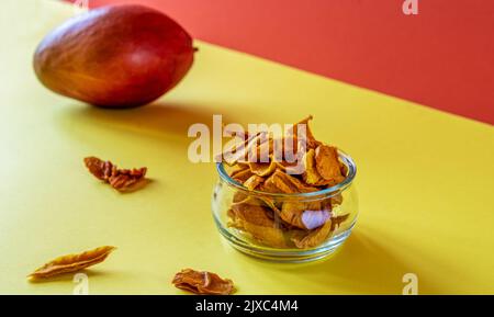 Mangochips in einem Glas auf gelbem und orangefarbenem Hintergrund Stockfoto