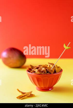Mangochips in Schüssel mit Spieß für Snack, rohe Mango auf gelbem und orangefarbenem Hintergrund Stockfoto