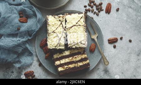 Kuchen mit Creme und dunklem Schokoladengebäck. Serviert in Quadraten auf einem Teller mit Kaffee in der Tasse Stockfoto