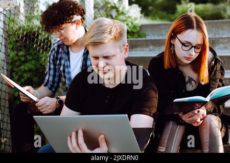 Drei junge, konzentrierte, ruhige Menschen, zwei Männer und eine rothaarige Frau in einer Brille, die am Laptop arbeitete und Bücher las. Hobby Stockfoto