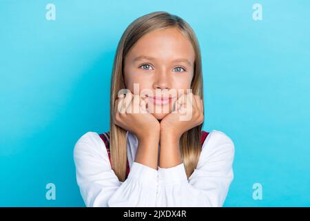 Nahaufnahme Foto von jungen kleinen niedlichen hübschen Schulmädchen berühren Wangen schönes Gesicht verträumt aussehen Sie isoliert auf blauem Hintergrund Stockfoto