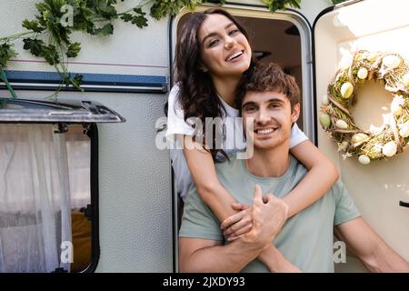 Positive Frau umarmt Freund in der Nähe Tür des Wohnmobil im Freien, Stock Bild Stockfoto