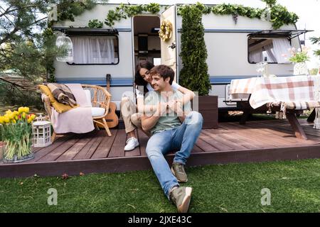 Lächelnde Frau umarmt Freund auf Terrasse in der Nähe von Wohnmobil im Freien, Stock Bild Stockfoto