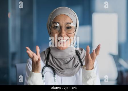 Webcam-Ansicht, arabische Ärztin in Hijab lächelnd und im Videoanruf sprechend, Kinderarzt spricht und Patient konsultiert, ferngesteuert im modernen Klinikbüro arbeitet. Stockfoto