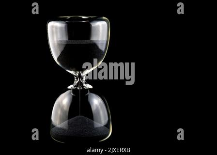 Sanduhr mit schwarzem Sand isoliert auf schwarzem Hintergrund Stockfoto