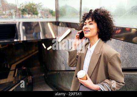 Lächelnde Frau, die sich am Telefon auf der Rolltreppe unterhielt Stockfoto