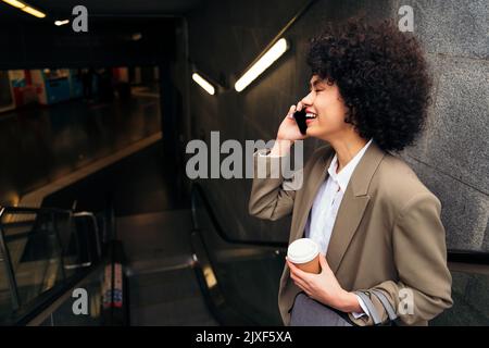 Eine Geschäftsfrau, die mit der Rolltreppe telefoniert Stockfoto