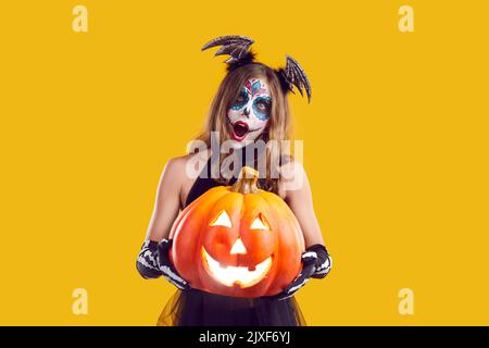 Mädchen in Halloween Kostüm hält Jack o Laterne und Blick auf die Kamera mit überraschter Ausdruck Stockfoto