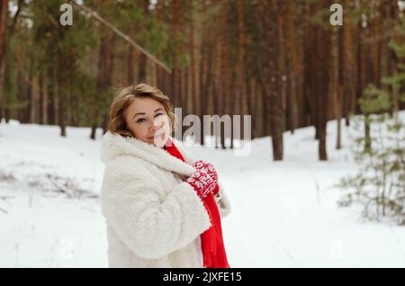Lustige alte Frau in Jeans, weißem Hut und Jacke in verschneiten Park, Wald. Mutter, die in der Nähe von schneebedeckten Pinien spazierengeht. Spaß haben. Winter mit der Familie Stockfoto