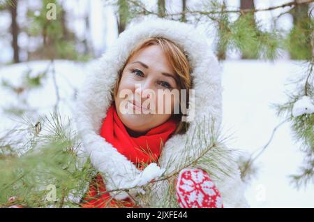 Lustige alte Frau in Jeans, weißem Hut und Jacke in verschneiten Park, Wald. Mutter, die in der Nähe von schneebedeckten Pinien spazierengeht. Spaß haben. Winter mit der Familie Stockfoto