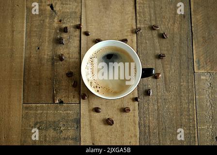 Holztisch mit Nahaufnahme von Kaffeetasse und Kaffeebohnen in Herzform Stockfoto