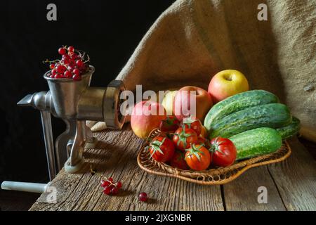 Reife Äpfel und Tomaten mit Gurken in einem Korb. Lebensmittel auf dem Hintergrund der Sackleinen. Sommerernte aus dem Garten und Gemüsegarten Stockfoto