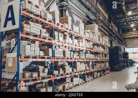 Industrieller Vertrieb, Zusammensetzung. Lagerung mit hohen Fachböden, Ladeboxen in Regalen. Reihen von Regalen mit Kästen im Werk. Stockfoto