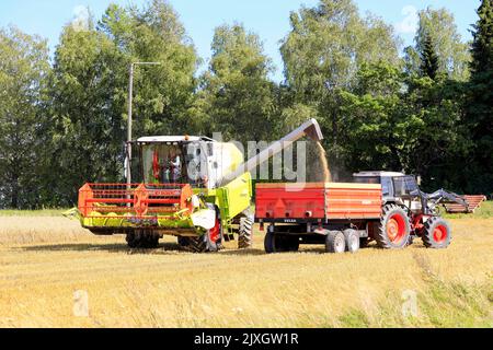 Claas Avero Combine Harvester entlädt den geernteten Hafer auf den landwirtschaftlichen Anhänger hinter dem Traktor David Brown/Case 1690. Salo, Finnland. 27. August 2022. Stockfoto