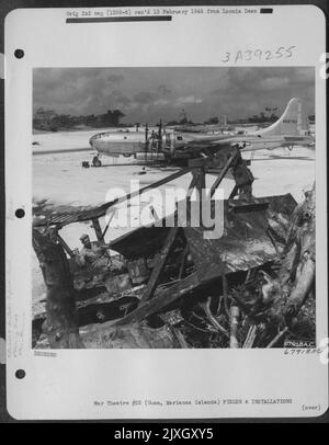 Ein Bulldozer, der von Einem Mitglied der Flugzeugingenieure betrieben wird, räumt den harten Standplatz für die Boeing B-29 „Superfortress“ frei. Im Hintergrund repariert Eine Bodenbesatzung zwei der Motoren auf einem der riesigen Flugzeuge, die auf Guam, den Marianas-Inseln, basieren, 24. März 1945. Stockfoto
