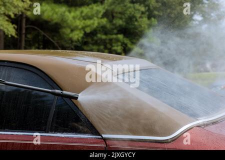 Ein Arbeiter wäscht sein Auto unter Hochdruckstrahl und spritzt Wasser darauf und reinigt es Stockfoto