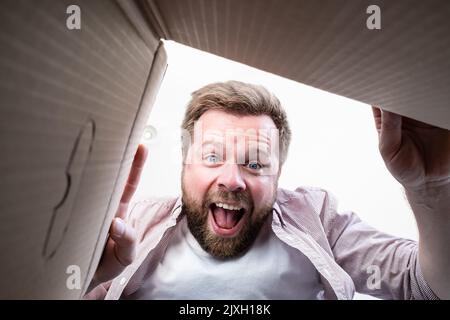 Glücklicher Mann packte die gelieferte Schachtel mit einem Paket aus und schreit freudig, als er den Inhalt ansah. Auspacken der Innenansicht. Stockfoto