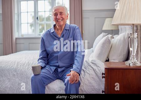 Älterer Mann Zu Hause Im Schlafanzug, Der Auf Dem Bett Sitzt Und Eine Tasse Tee Am Morgen Serviert Stockfoto