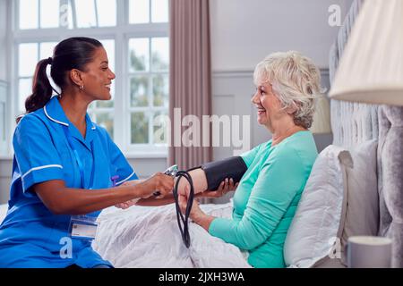 Ältere Frau Zu Hause Im Bett, Die Von Einer Weiblichen Pflegekraft In Uniform Den Blutdruck Genommen Hat Stockfoto