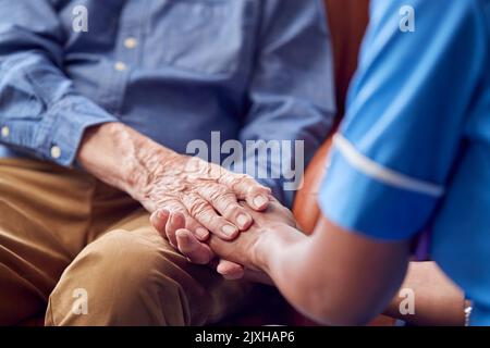 Nahaufnahme Einer Weiblichen Pflegekraft In Uniform Holding Hands Eines Älteren Mannes, Der In Der Care Home Lounge Sitzt Stockfoto