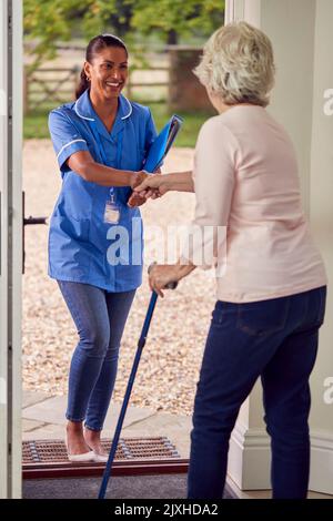 Ältere Frau Zu Hause Mit Gehstock Gruß Weibliche Krankenschwester Oder Pflegekraft In Uniform An Der Tür Stockfoto