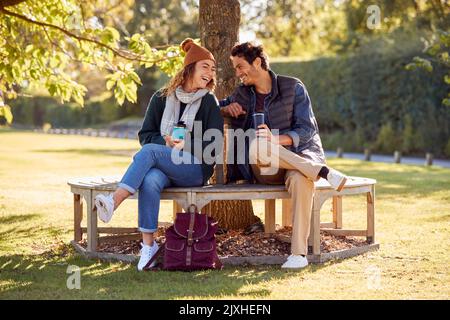 Lächelndes Paar Sitzt Auf Der Bank Im Herbst Park Mit Wiederverwendbaren Getränkebecher Stockfoto