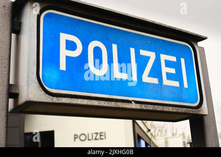 Ein blaues Schild mit der Aufschrift „Poizei“ für „Polizei“ auf einer deutschen Polizeistation. Das Wort steht auch auf dem Gebäude im Hintergrund. Bild aufgenommen Stockfoto