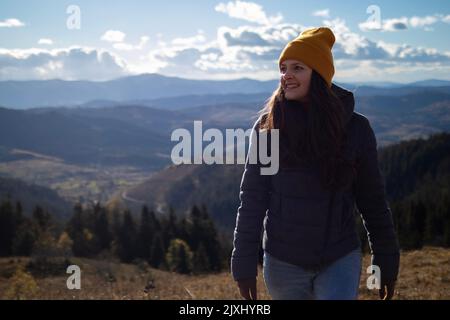 Junge glückliche Frau in orangefarbener Mütze läuft vor der Berglandschaft Stockfoto