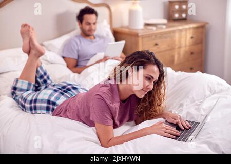 Paar Tragen Pyjamas Liegen Im Bett Zu Hause Mit Frau Mit Laptop Und Mann Digital Tablet Stockfoto