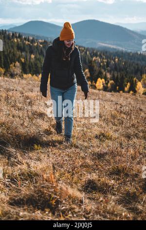 Junge glückliche Frau in orangefarbener Mütze läuft vor der Berglandschaft Stockfoto