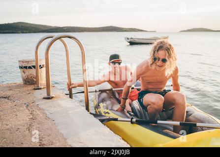 Vater mit Teenager-Sohn auf dem leuchtend gelben aufblasbaren Kajak, der von der Abendfahrt am Adriatischen Hafen in Kroatien in der Nähe von Sibeni zurückkehrt Stockfoto