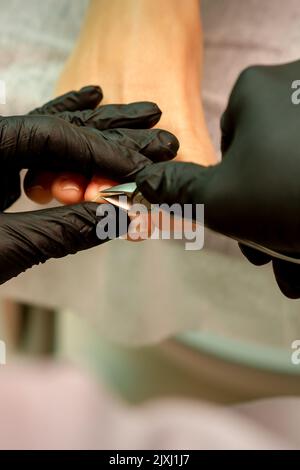 Professionelle Pediküre. Pediküre Master trägt Latexhandschuhe schneidet weibliche Fußnägel im Schönheitssalon, Nahaufnahme Stockfoto