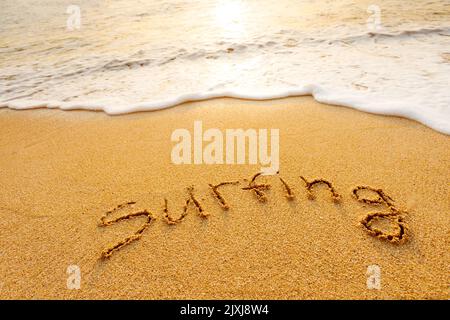 Das Wort Surfen steht im Sand am Strand Stockfoto