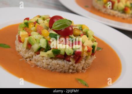 Veganes Salatrezept auf Basis von Bulgur mit kleinem Gemüse, Avocado, Tomaten, Gurken, Pfeffer, Nektarinfrüchte, Tomatenbasilsauce Stockfoto