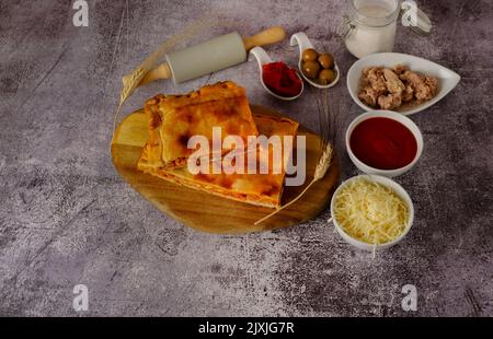 Thunfisch-Empanada mit allen Zutaten in Keramikbehältern im Boden einer roten Ziegelwand getrennt Stockfoto