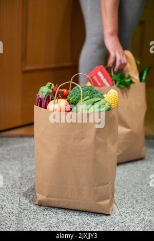 Eine Frau nimmt eine Tüte mit Essen vor der Tür ihres Hauses. Coronavirus. Quarantäne. Bleiben Sie zu Hause, Online-Shopping. Gemüse und Obst Lieferung während Stockfoto