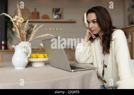 Eine junge Frau, die am Tisch sitzt, schaut aus erster Hand in den Laptop Stockfoto