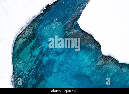 Eine malerische Aussicht von oben auf den kristallklaren blauen Fluss mit schneebedeckten Flussufern Stockfoto