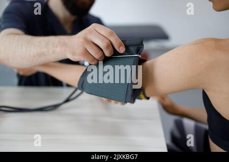 Nahaufnahme eines Arztes, der die Manschette eines Blutdruckmessers auf den Arm einer Frau legt. Weibliche Patientin auf ärztliche Untersuchung Stockfoto