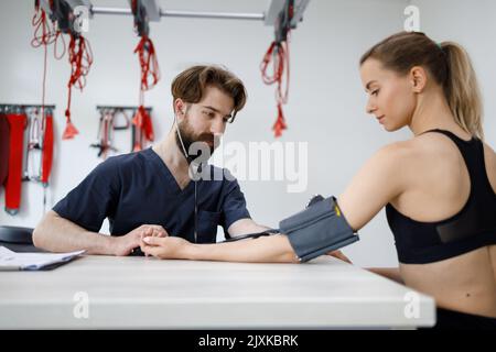 Der Arzt misst den Blutdruck bei einer jungen Sportlerin Stockfoto