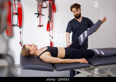 Chiropraktiker streckt ein weibliches Bein. Der männliche Physiotherapeut hilft der Frau, ihr Bein im Fitnessraum zu strecken Stockfoto