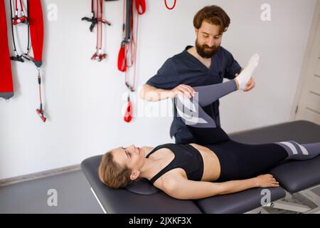 Physiotherapeutin, die mit den Beinen einer jungen Patientin im Rehabilitationszentrum arbeitet Stockfoto