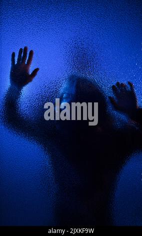 Schatten einer Frau, die hinter dem Glas schreit, Konzept der häuslichen Gewalt. Stockfoto